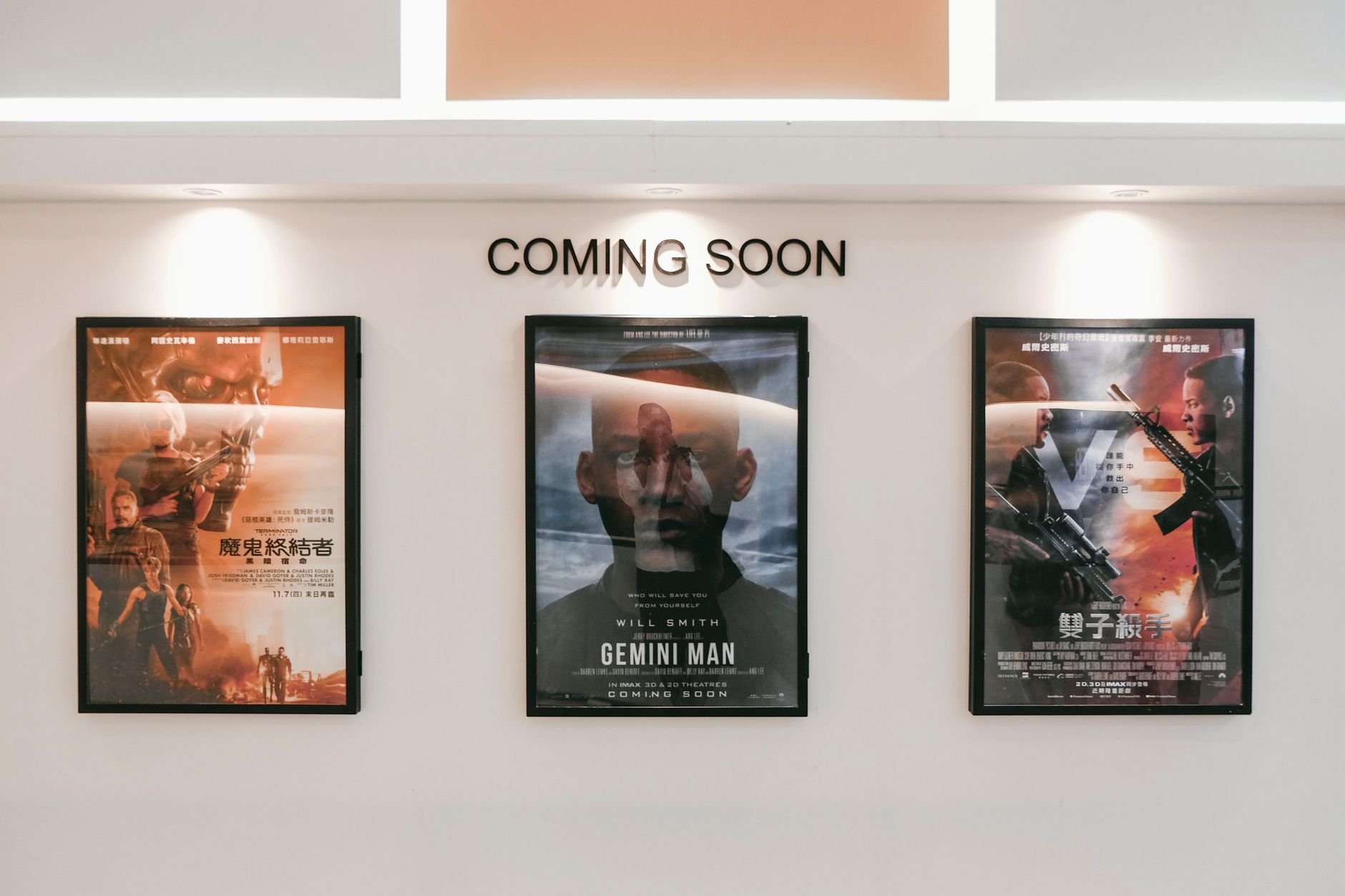 Framed posters of upcoming movies in a cinema hallway under a Coming Soon sign